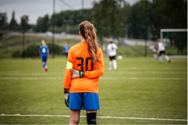 Girl goalkeeper looking at football pitch